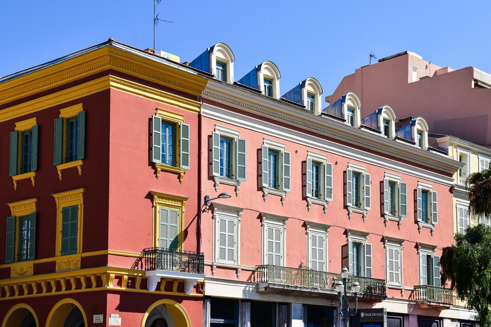 Alignement de façades ocre et rose aux volets peints